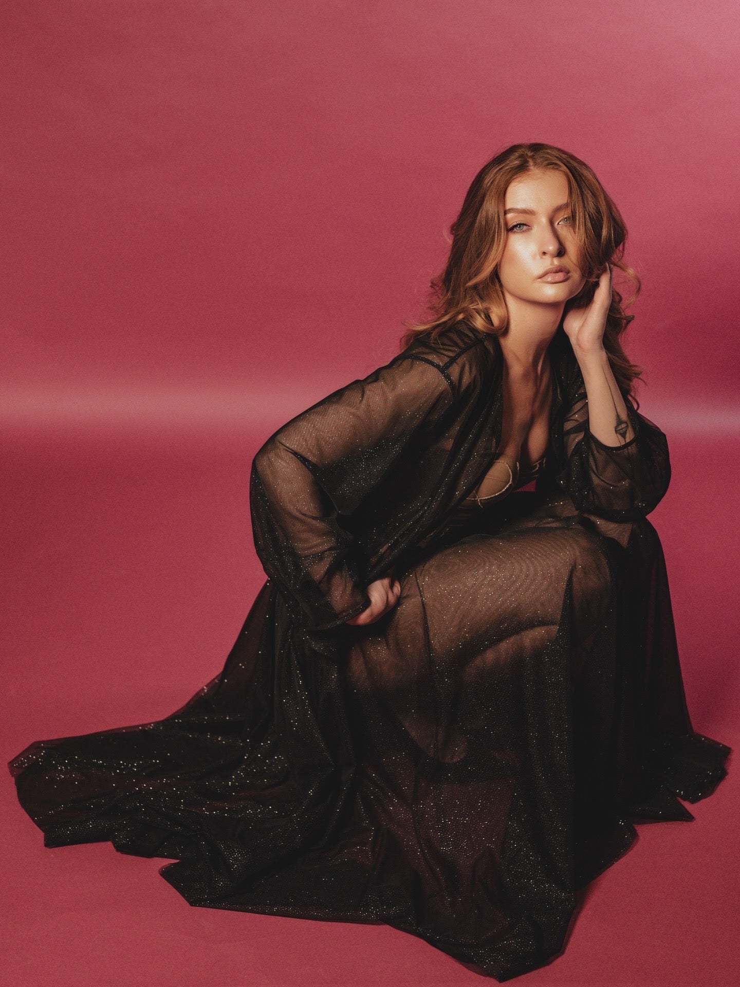 Woman in a black sheer Mai Attire skirt and jacket sitting against a pink background